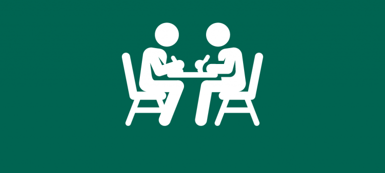 Pictogram: 2 Personen sitzen sich an einem Tisch gegenüber und schreiben etwas auf